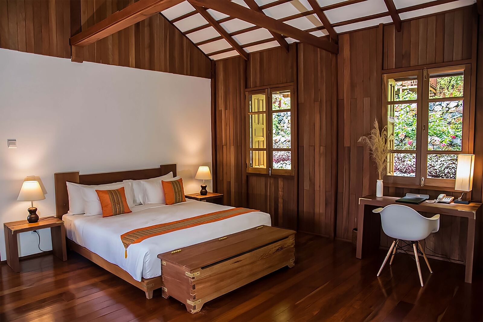 Guest room with wood-panelled walls, a king bed, orange cushions, and a writing desk