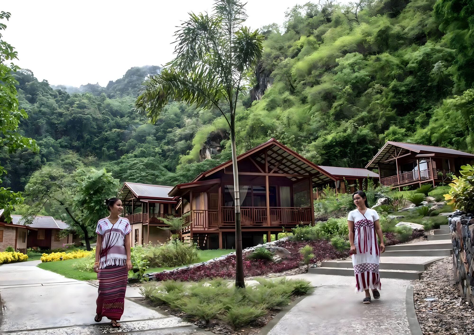 Two women in Karen dress on the path in front of the wooden cottages at Keinnara Hpa-An